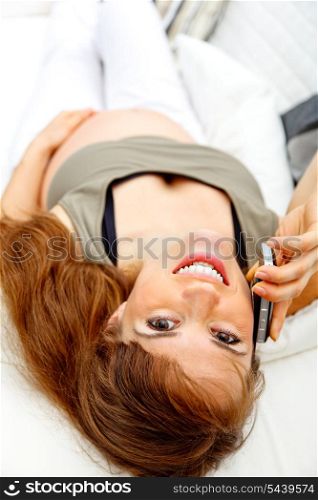 Smiling beautiful pregnant woman relaxing on couch at home and talking mobile.&#xA;