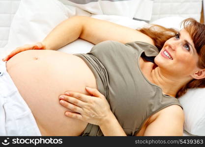 Smiling beautiful pregnant woman relaxing on couch at home and touching her tummy. Closeup.&#xA;