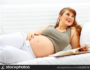 Smiling beautiful pregnant woman relaxing on couch at home with book.&#xA;