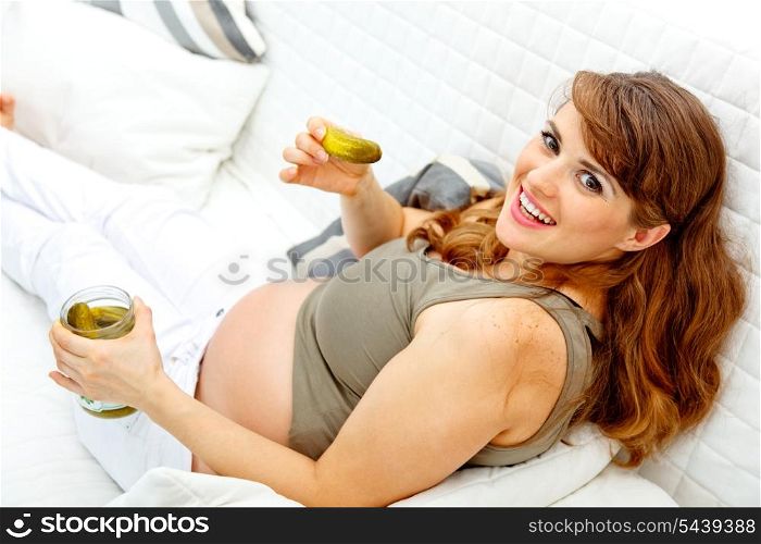 Smiling beautiful pregnant woman relaxing on sofa at home and eating pickles&#xA;