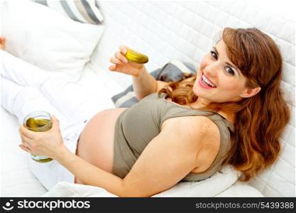 Smiling beautiful pregnant woman relaxing on sofa at home and eating pickles&#xA;