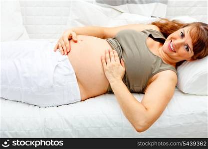 Smiling beautiful pregnant woman relaxing on sofa at home and holding her tummy.&#xA;