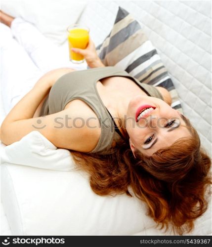 Smiling beautiful pregnant woman relaxing on sofa at home with glass of juice in hand&#xA;