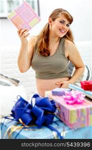Smiling beautiful pregnant woman sitting on couch at home with gifts for her unborn baby&#xA;