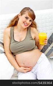 Smiling beautiful pregnant woman sitting on couch at home with glass of juice in hand&#xA;