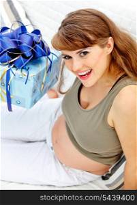 Smiling beautiful pregnant woman sitting on couch with present for her unborn baby&#xA;