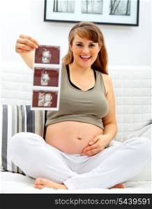 Smiling beautiful pregnant woman sitting on divan at home with echo in hand.&#xA;