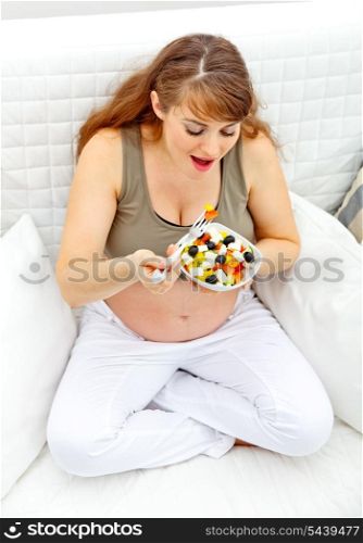 Smiling beautiful pregnant woman sitting on sofa at home and eating fresh vegetable salad&#xA;