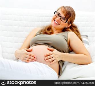 Smiling beautiful pregnant woman sitting on sofa at home and holding her belly&#xA;