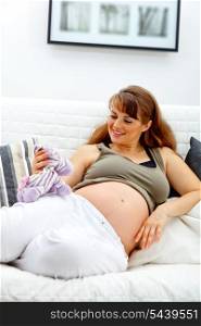 Smiling beautiful pregnant woman sitting on sofa at home and holding toy &#xA;