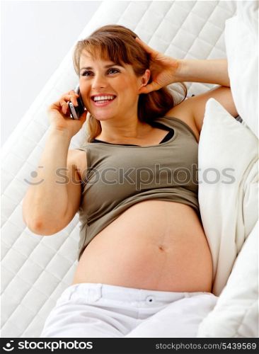 Smiling beautiful pregnant woman sitting on sofa at home and talking mobile phone.&#xA;