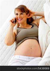 Smiling beautiful pregnant woman sitting on sofa at home and talking mobile phone.&#xA;