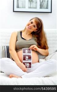 Smiling beautiful pregnant woman sitting on sofa at home with echo in hand.&#xA;