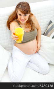 Smiling beautiful pregnant woman sitting on sofa at home with glass of juice in hand. Close-up.&#xA;