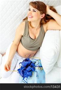 Smiling beautiful pregnant woman sitting on sofa with present for her unborn baby&#xA;