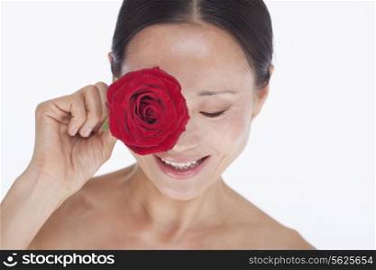 Smiling, beautiful, shirtless woman holding a red rose to her eye, studio shot