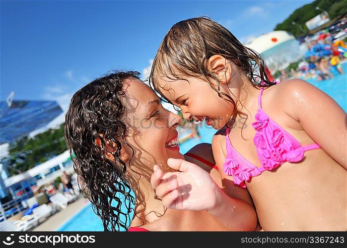 Smiling beautiful woman and little girl bathing in pool of an entertaining complex, concerning with heads