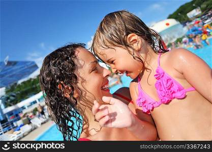 Smiling beautiful woman and little girl bathing in pool of an entertaining complex, concerning with heads