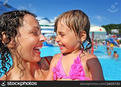 Smiling beautiful woman and little girl bathing in pool of an entertaining complex, Looking against each other