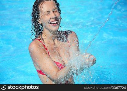 Smiling beautiful woman bathes in pool under water splashes, closed eyes
