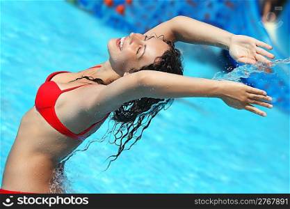 Smiling beautiful woman bathes in pool under water stream, lifted hands upwards