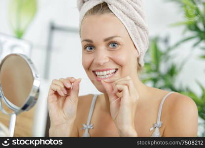 smiling beautiful woman in bath towel using a dental floss