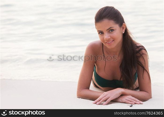Smiling beautiful woman in bikini lying on beach at sunset time. Smiling woman lying on beach