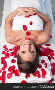 Smiling beautiful woman lying on a massage table with rose petals around