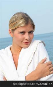 Smiling beautiful woman standing by the sea in bathrobe