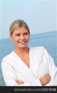 Smiling beautiful woman standing by the sea in bathrobe