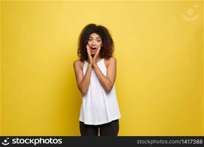 Smiling beautiful young African American woman in white T-shirt posing with hands on chin. Studio shot on Yellow background. Copy Space. Smiling beautiful young African American woman in white T-shirt posing with hands on chin. Studio shot on Yellow background. Copy Space.