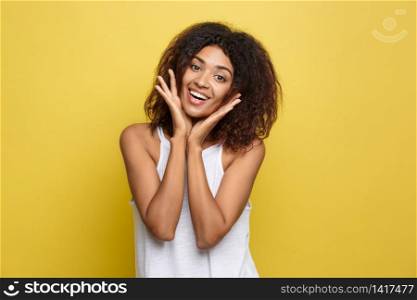 Smiling beautiful young African American woman in white T-shirt posing with hands on chin. Studio shot on Yellow background. Copy Space. Smiling beautiful young African American woman in white T-shirt posing with hands on chin. Studio shot on Yellow background. Copy Space.