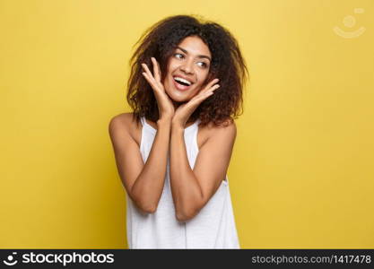 Smiling beautiful young African American woman in white T-shirt posing with hands on chin. Studio shot on Yellow background. Copy Space. Smiling beautiful young African American woman in white T-shirt posing with hands on chin. Studio shot on Yellow background. Copy Space.