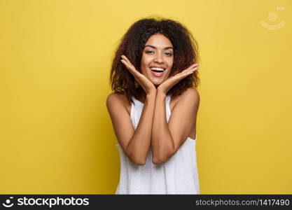 Smiling beautiful young African American woman in white T-shirt posing with hands on chin. Studio shot on Yellow background. Copy Space. Smiling beautiful young African American woman in white T-shirt posing with hands on chin. Studio shot on Yellow background. Copy Space.