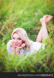Smiling beautiful young woman lying among the green grass