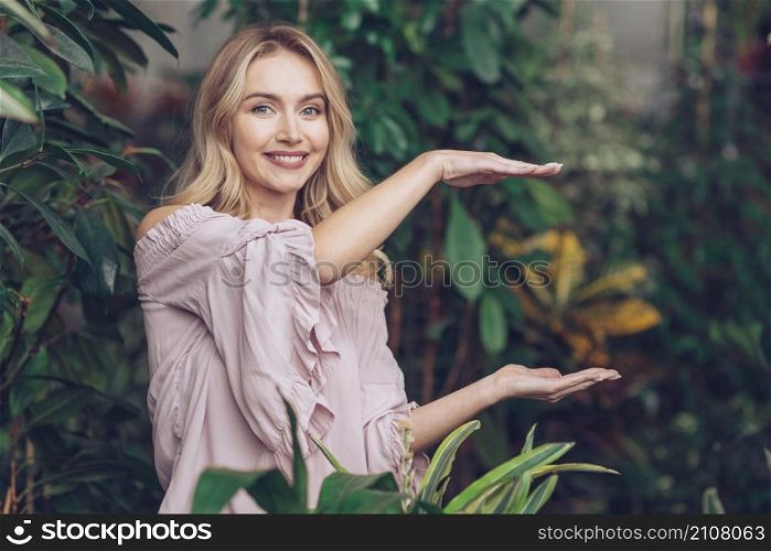smiling beautiful young woman showing something palms her hands garden