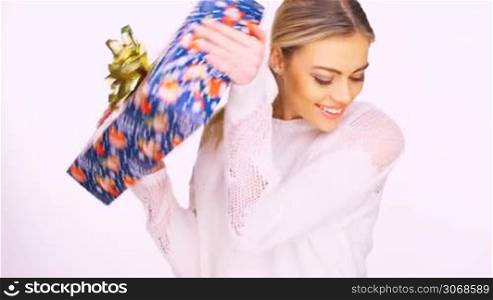 Smiling beautiful young woman with a colourful Christmas gift decorated with a golden bow clutched in her arms, isolated on white