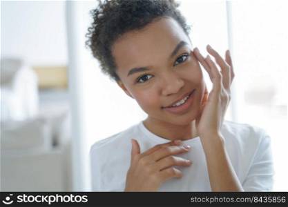 Smiling biracial teen girl apply moisturizing face cream or serum for healthy skin, happy young mixed race woman perform daily morning facial care. Skincare beauty treatment cosmetics advertising.. Biracial teen girl applying facial cosmetic serum for healthy face skin. Skincare beauty treatment