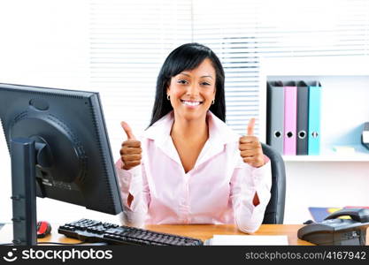 Smiling black business woman giving thumbs up gesture at desk in office