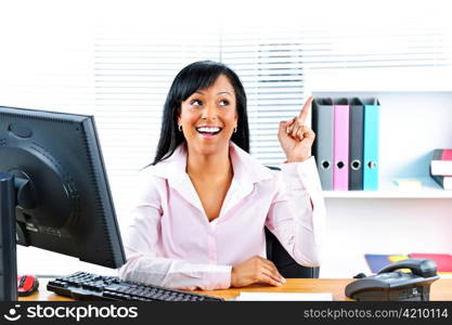 Smiling black business woman pointing up with idea at desk in office