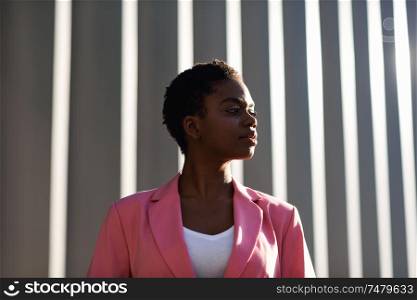 Smiling black businesswoman standing near business office building. African american female wearing suit with pink jacket.. Smiling black businesswoman standing near business office building