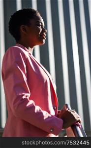 Smiling black businesswoman standing near business office building. African american female wearing suit with pink jacket.. Smiling black businesswoman standing near business office building