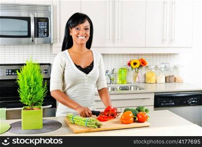 Smiling black woman cutting vegetables in modern kitchen interior