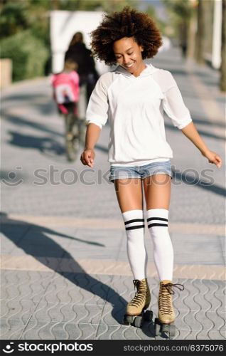 Smiling black woman on roller skates riding outdoors on beach promenade with palm trees. Smiling girl with afro hairstyle rollerblading on sunny day.