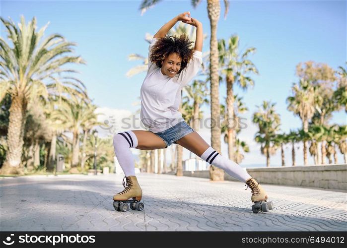Smiling black woman on roller skates riding outdoors on beach promenade with palm trees. Smiling girl with afro hairstyle rollerblading on sunny day.. Black woman on roller skates rollerblading in beach promenade wi