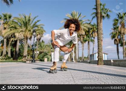Smiling black woman on roller skates riding outdoors on beach promenade with palm trees. Smiling girl with afro hairstyle rollerblading on sunny day.. Black woman on roller skates rollerblading in beach promenade wi