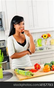 Smiling black woman tasting vegetables in modern kitchen interior