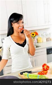 Smiling black woman tasting vegetables in modern kitchen interior