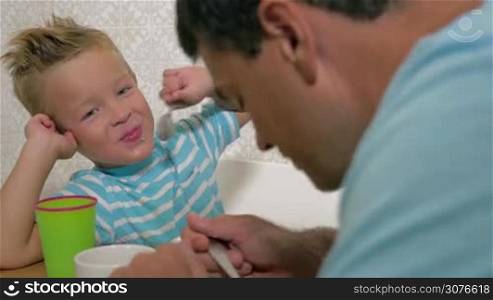 Smiling blond boy speaking with father eat using a spoon and be naughty close up view