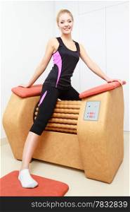 Smiling blond girl in sportwear using modern relax massage equipment. Young woman doing relaxation exercise in healthy spa salon.